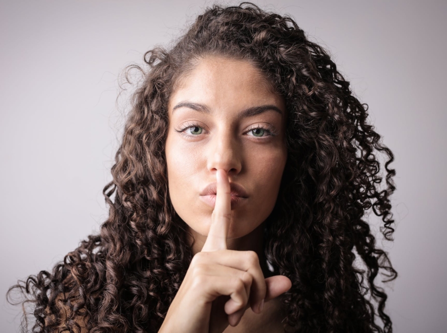 portrait photo of woman with brown curly hair doing the shhh sign