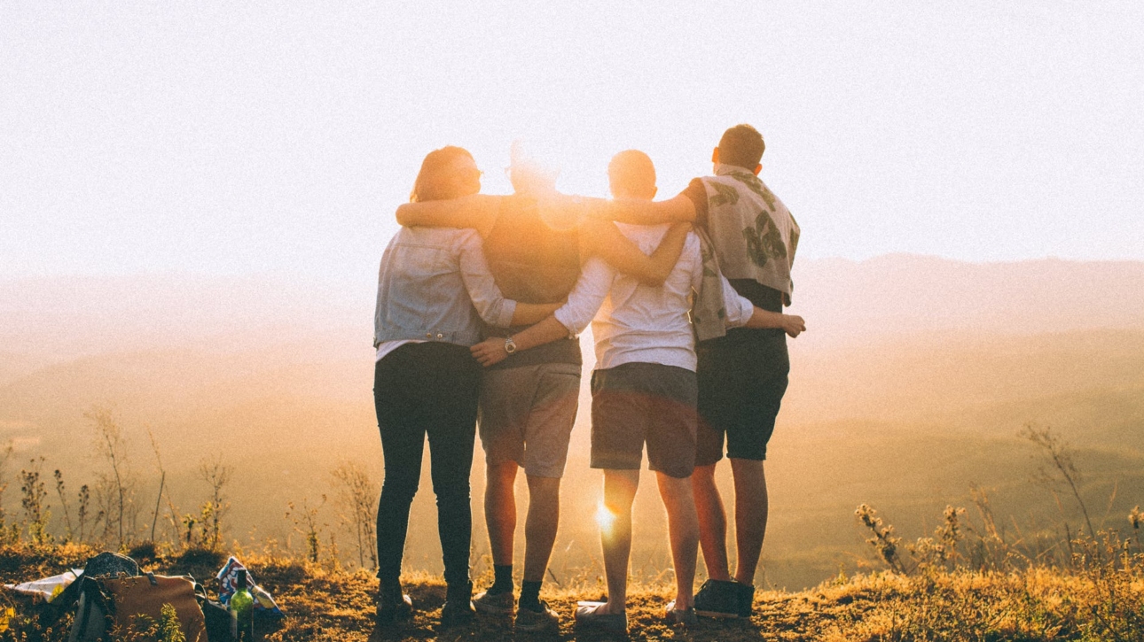 four person standing on cliff in front of sun