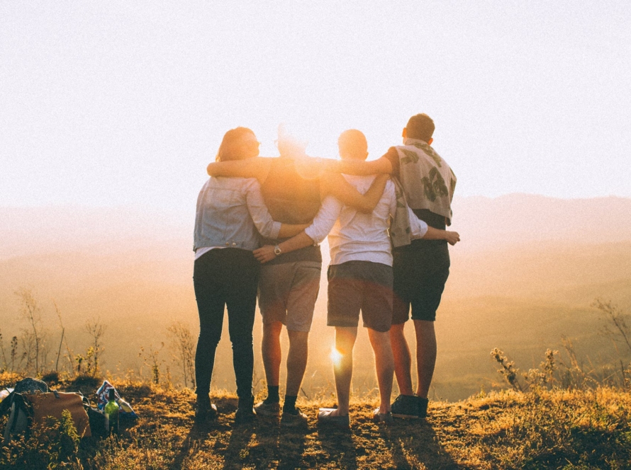 four person standing on cliff in front of sun