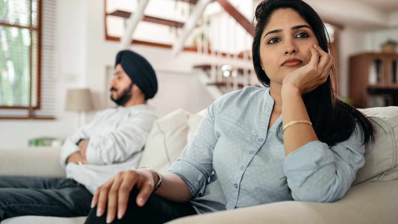 sad young indian woman avoiding talking to husband while sitting on sofa